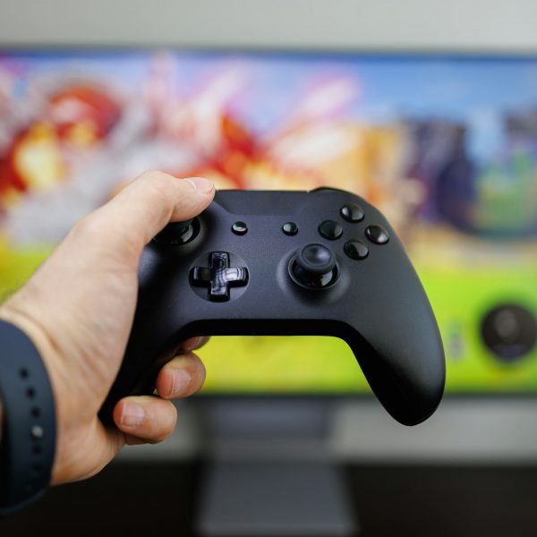 A hand holds a game controller in front of the monitor, Video game gamepad in hand